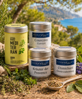 Schuhbecks Sommer-Mediterran-Set: die vier Gewürzdosen Mediterran Gewürzsalz, Couscous-Gewürz, Kräuter der Provence und Chimichurri vor mediterraner Küstenlandschaft